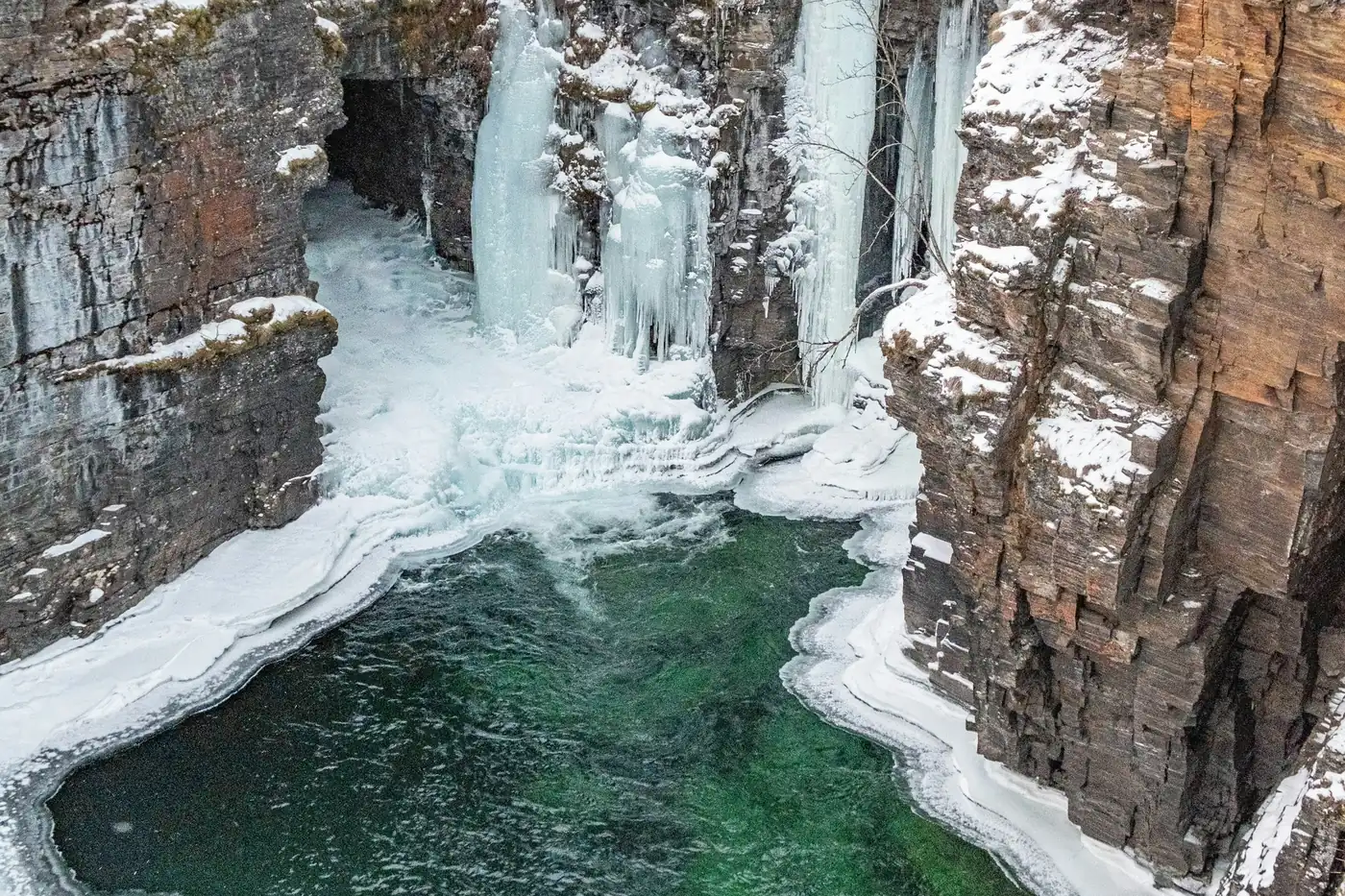 Cañón rocoso en invierno con cascadas heladas y una poza verde parcialmente cubierta de hielo
