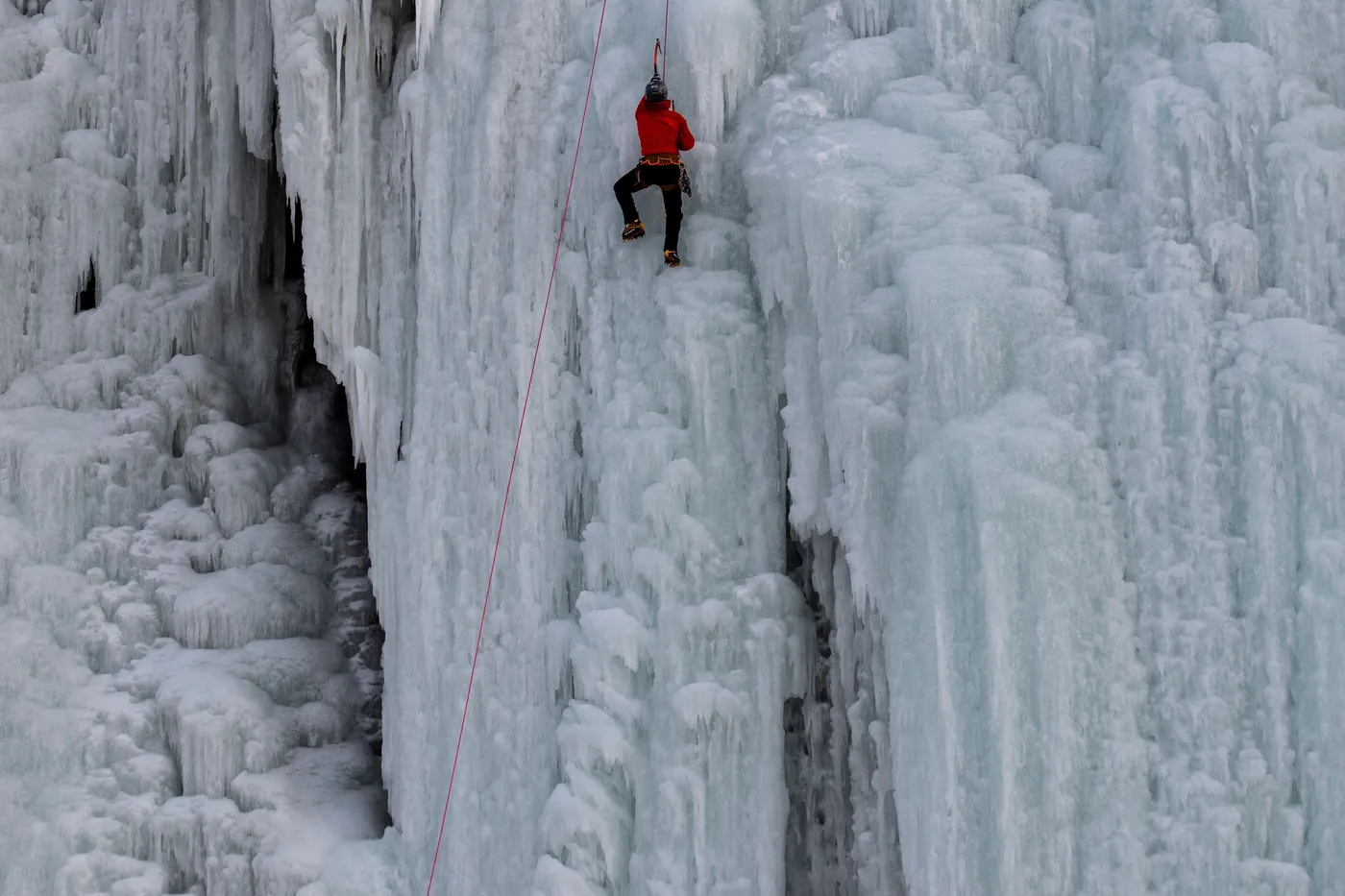 Eiskletterer in roter Jacke an einem riesigen gefrorenen Wasserfall mit Eiszapfensäulen